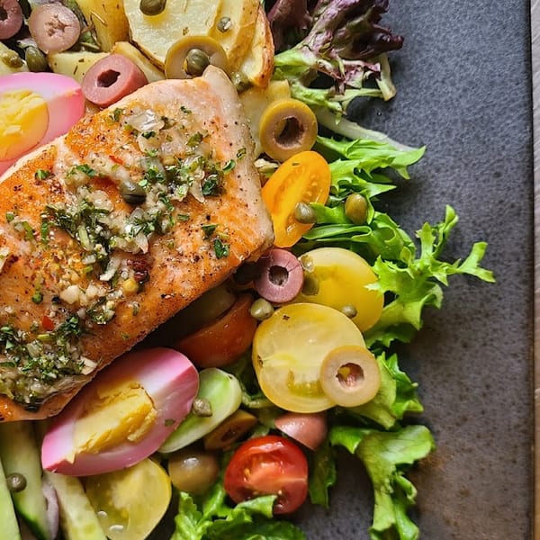 Grilled salmon with green beans, olives, tomatoes, and pickled eggs on a dark plate.