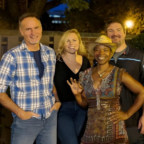 Four smiling people, two men and two women, pose together outdoors at night.