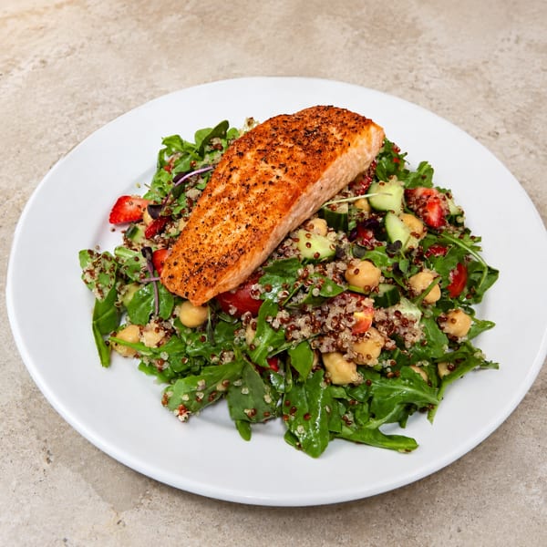 Grilled salmon fillet on a fresh salad with arugula, quinoa, chickpeas, strawberries, and cucumbers.