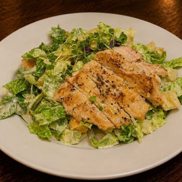 Grilled chicken Caesar salad with croutons and microgreens on a white plate.