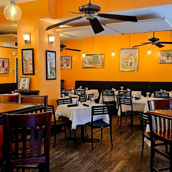 Vibrant orange walls, dark wood floors, and white-clothed tables fill a cozy restaurant dining room.