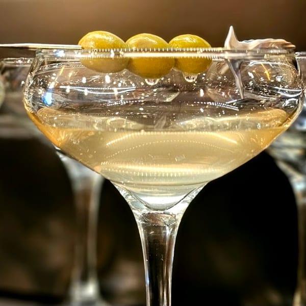 A martini glass filled with a clear drink and three green olives on a skewer.